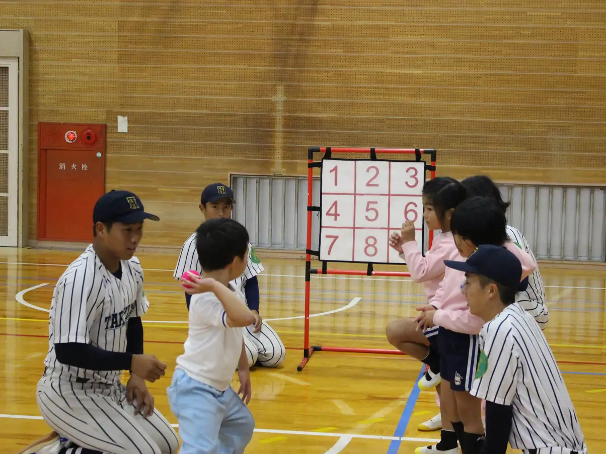 野球部員と一緒に的を狙ってボールを投げる園児
